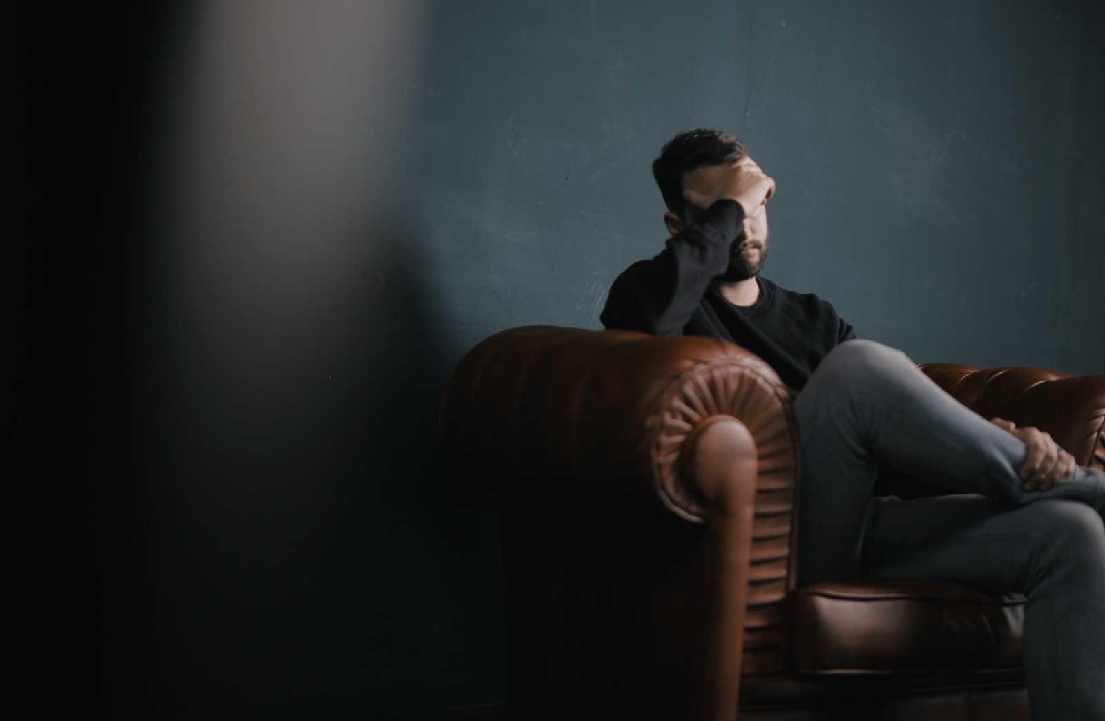 a man holds his head in stress while sitting on a sofa